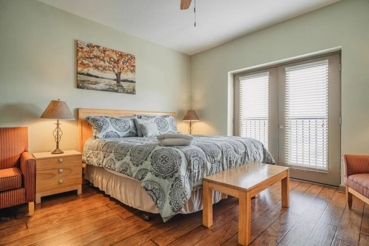 A sunlit bedroom featuring a plush bed with decorative bedding, inviting wooden furniture, and artwork that adds a personal touch. Sliding glass doors let in natural light, creating a warm and cozy atmosphere perfect for relaxation after a day exploring the Smoky Mountains.
