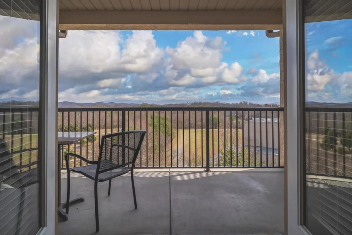 This image shows a tranquil balcony scene with a sturdy railing, a table and chair, all overlooking breathtaking mountain views. The setting is ideal for sipping morning coffee, relaxing with a book, or enjoying the natural beauty at sunrise or sunset.