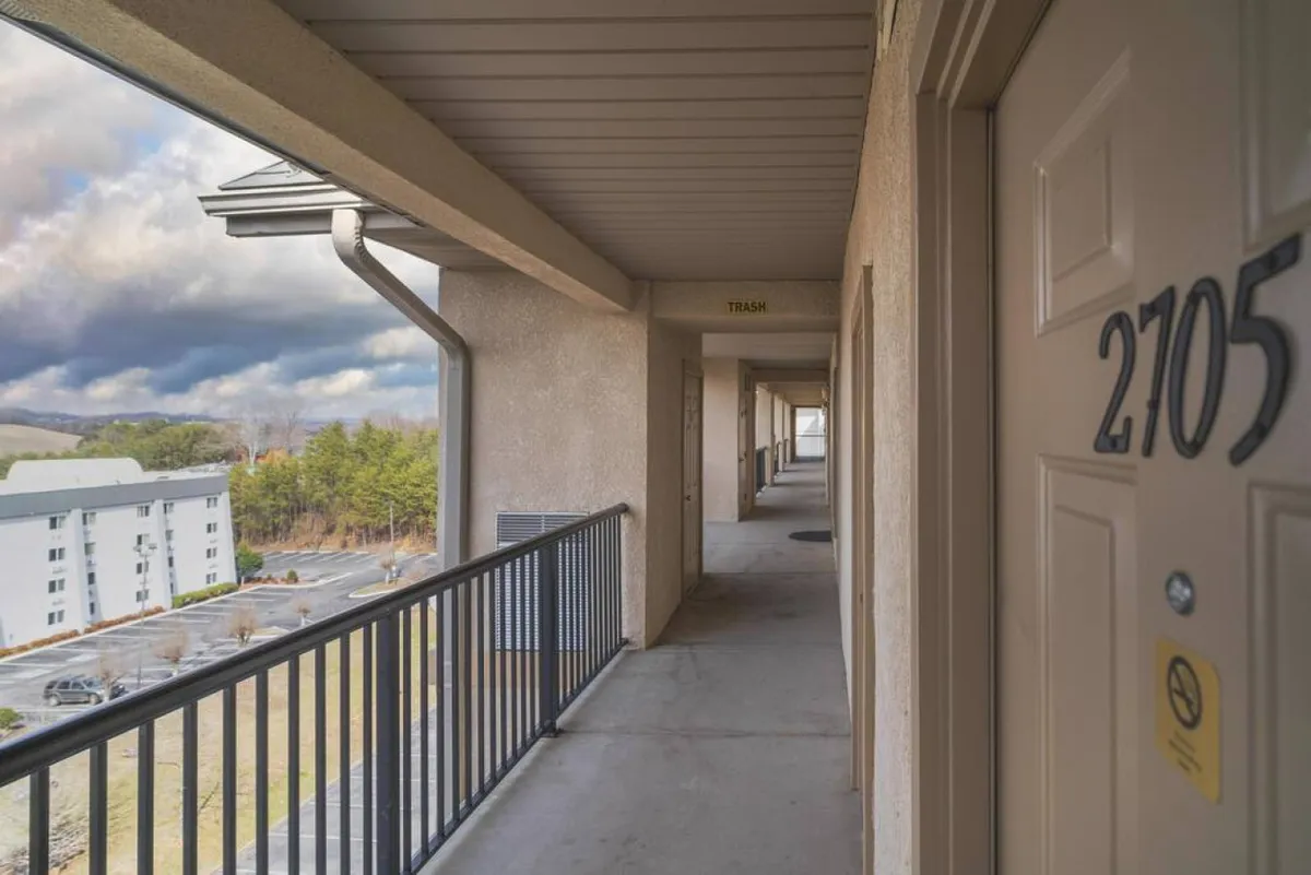This exterior image shows the corridor leading to unit 2705, with a clear view of the balcony railing and the parking lot beyond. A guest can be seen either walking down the corridor or enjoying a moment on the balcony, suggesting the ease of stepping outside and taking in the surroundings. The vantage point hints at an elevated position, likely offering broader views from the balcony.