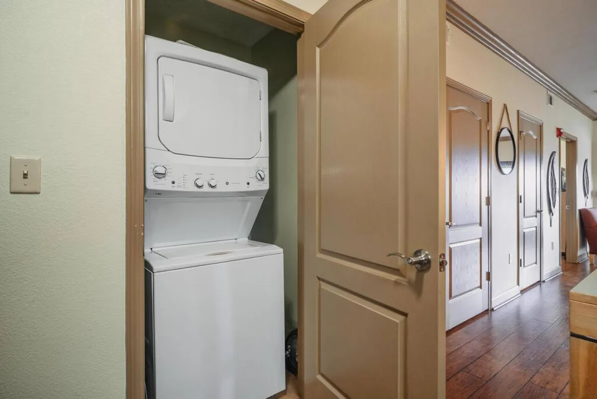 A practical corner featuring a stacked washer and dryer, adjacent to a doorway with wood flooring. The laundry appliances are neatly integrated for convenience, suggesting ease of use during longer stays.