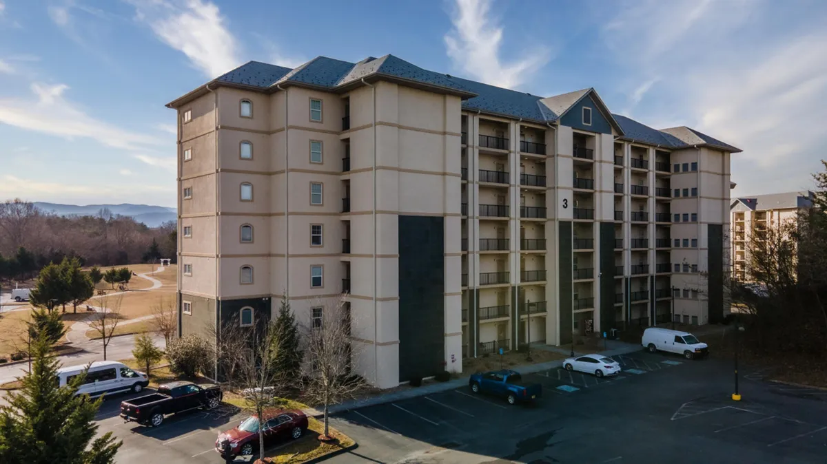 This exterior image shows the condo building's welcoming facade, adjacent parking lot, and well-kept surrounding landscape. The scene evokes a sense of arrival and community, with hints of the neighborhood's energy and accessibility.