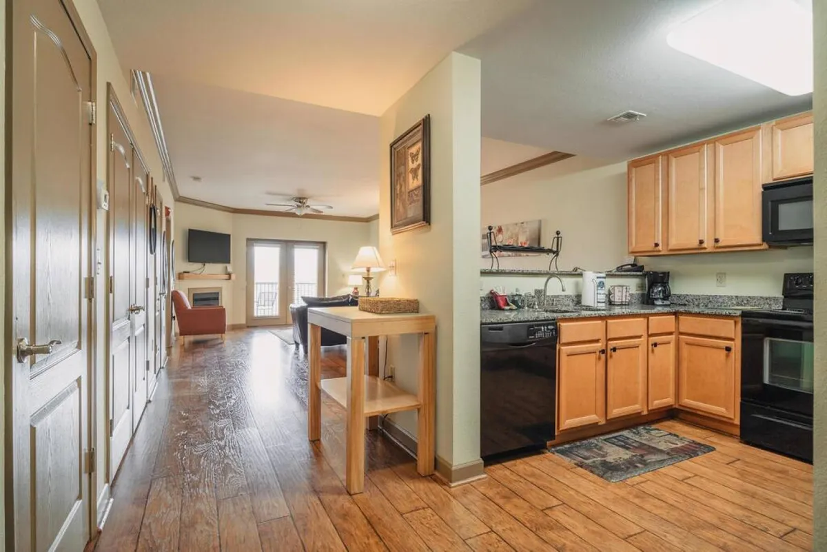 This image features a view of the kitchen area seamlessly connected to the living room seating, with a doorway leading outside. The space is cozy and inviting, showcasing comfortable sofas and a practical, open layout that encourages gathering and interaction.