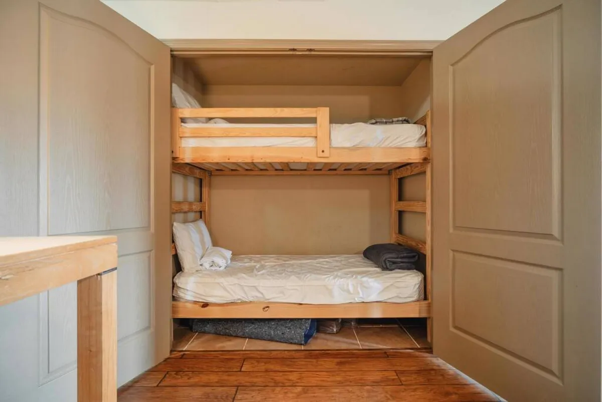 The image displays a pair of twin bunk beds within a wooden-framed 'bunk closet,' neatly arranged with fresh bedding. The cozy nook exudes a sense of comfort, making it ideal for children or extra guests to have their special retreat close to the action.